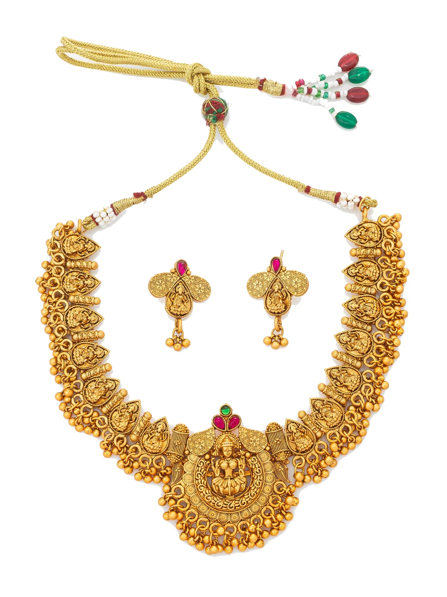 An ornate gold-toned jewelry set featuring a heavily decorated necklace with a central deity pendant, matching earrings, and a cord closure with red and green bead accents, displayed on a plain white background.