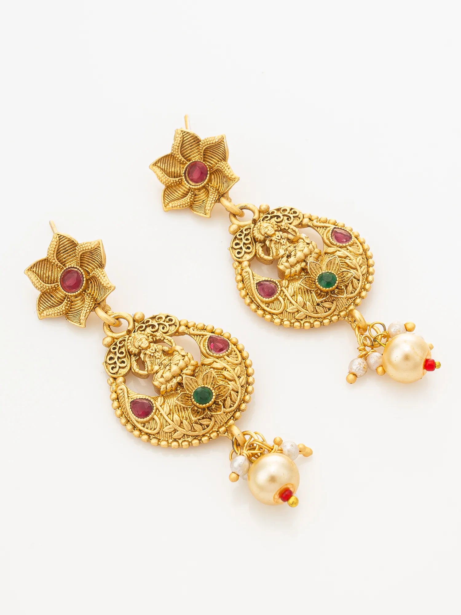 A pair of gold-plated Indian jhumka earrings with detailed filigree, red and green stone accents, and dangling pearl beads on a plain white background.