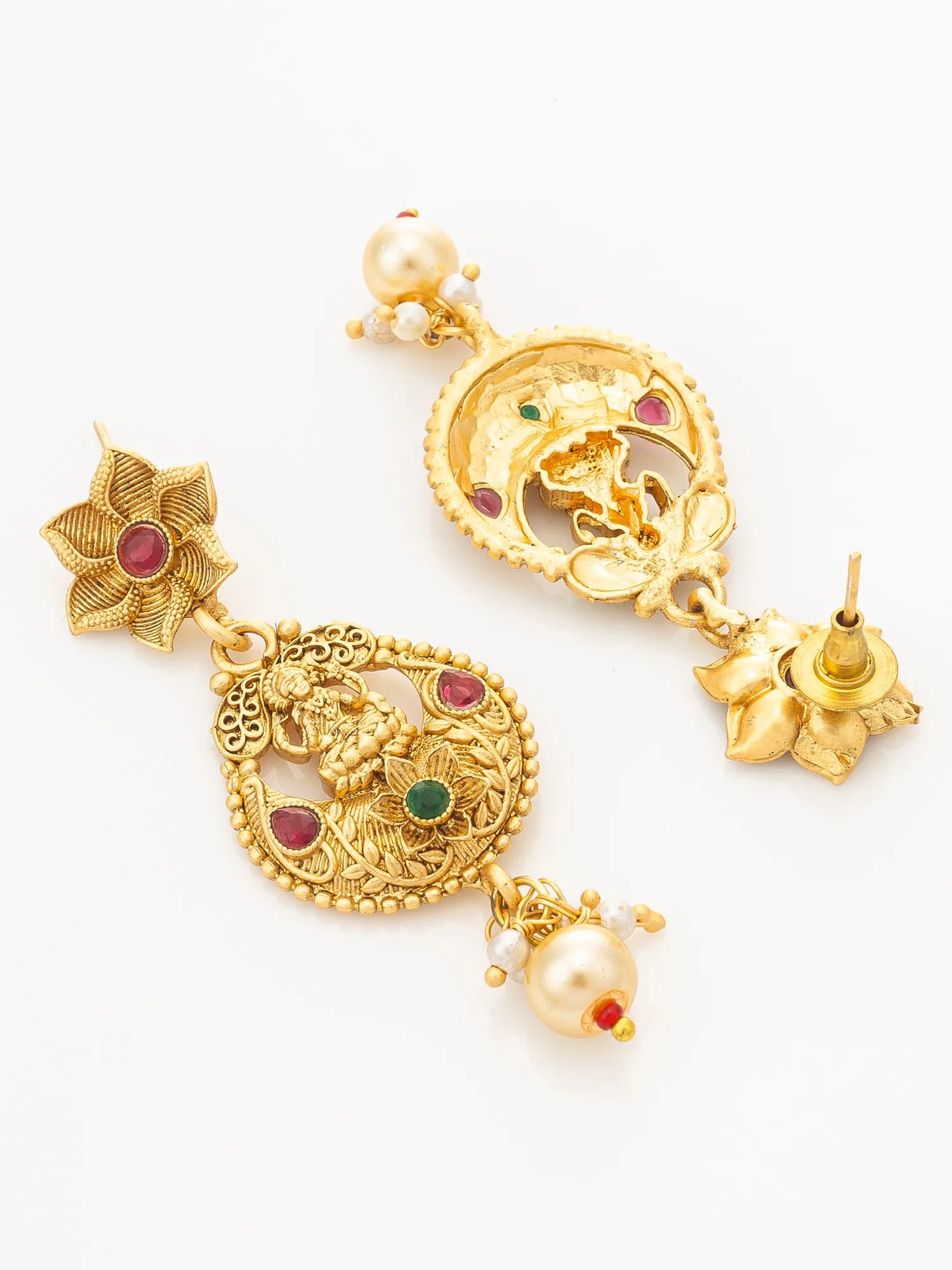 A pair of ornate gold-toned traditional earrings with carved filigree, small red and green stone accents, and pearl-like bead drops, photographed on a clean white background.