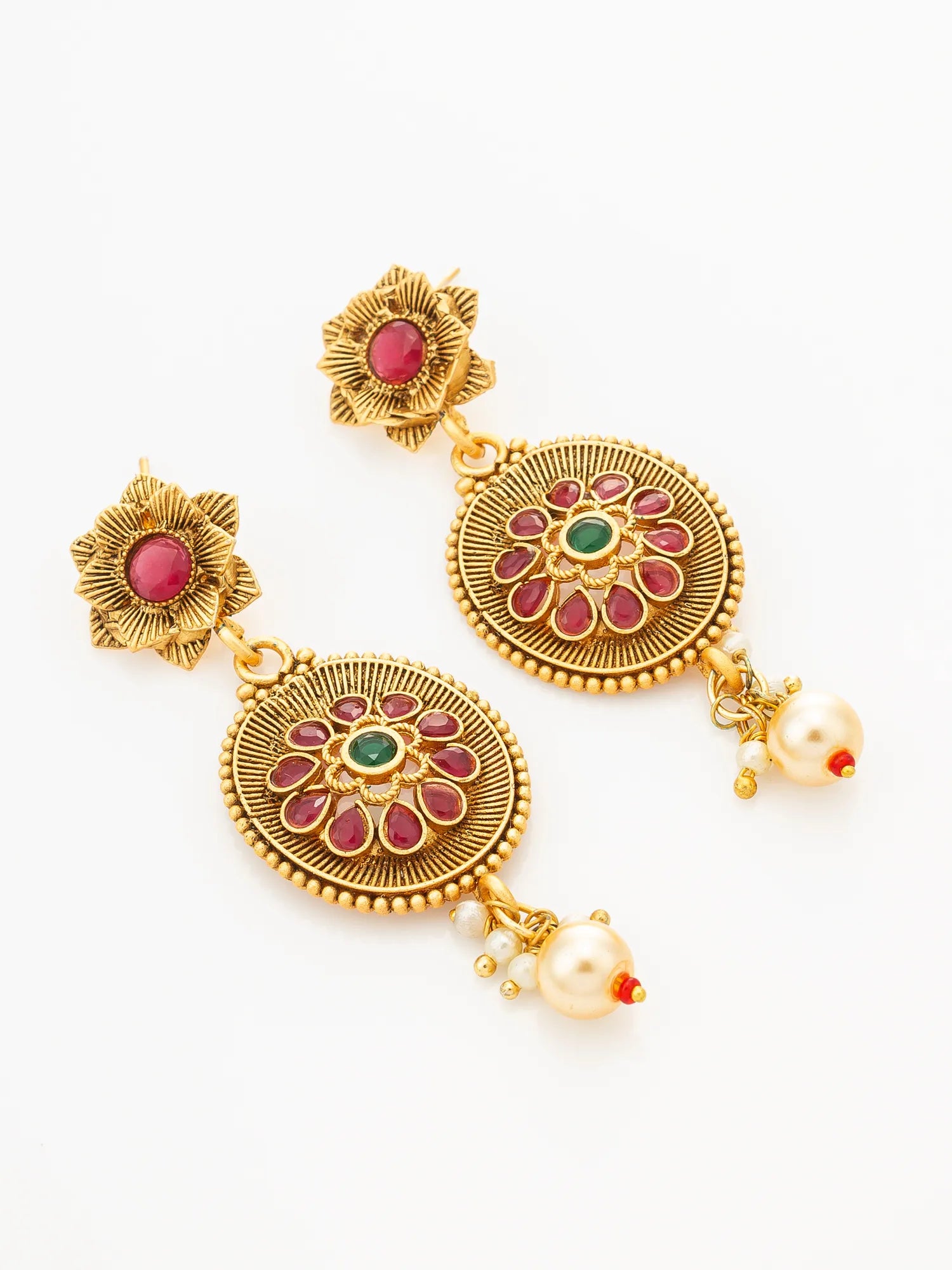 A pair of gold-toned traditional Indian dangle earrings with red and green stone accents and pearl-like drops, displayed on a clean white background.