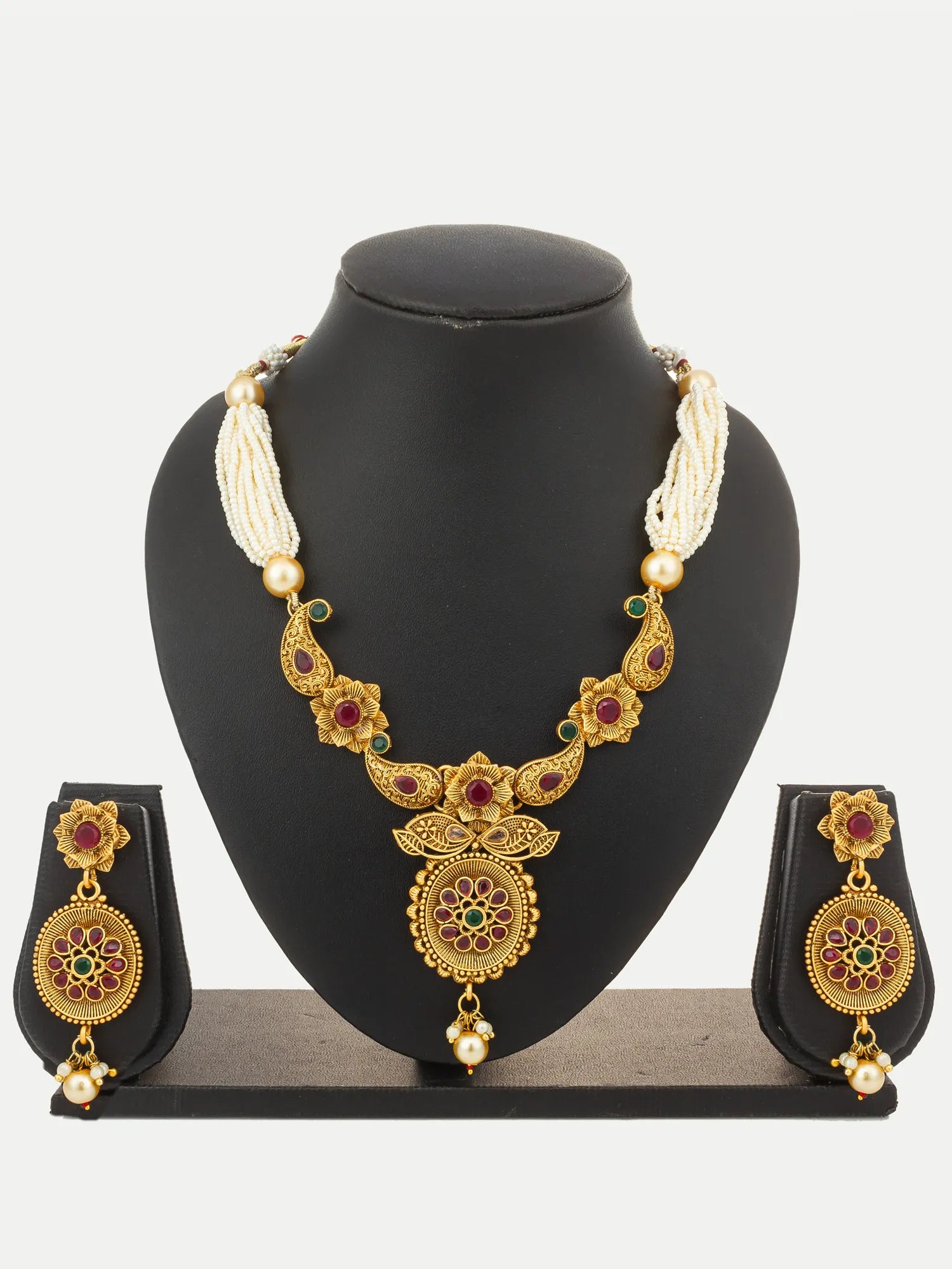 Gold-toned traditional jewelry set displayed on a black mannequin bust, including a necklace with cream bead strands and matching drop earrings, decorated with red and green stone accents.