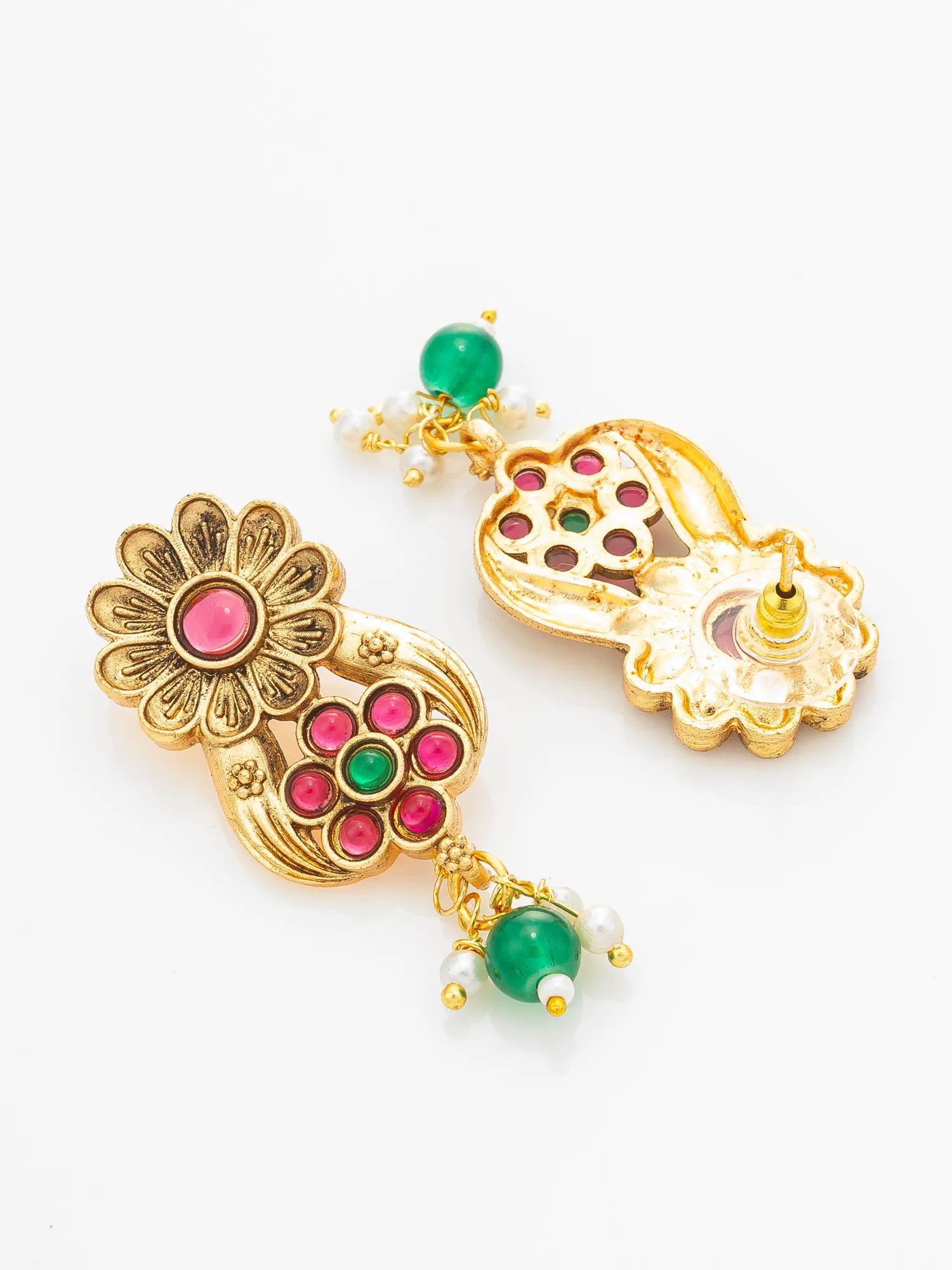 A pair of ornate gold-toned Indian jhumka earrings decorated with pink and green stones, featuring a floral motif and dangling green bead charms, set against a plain white background.