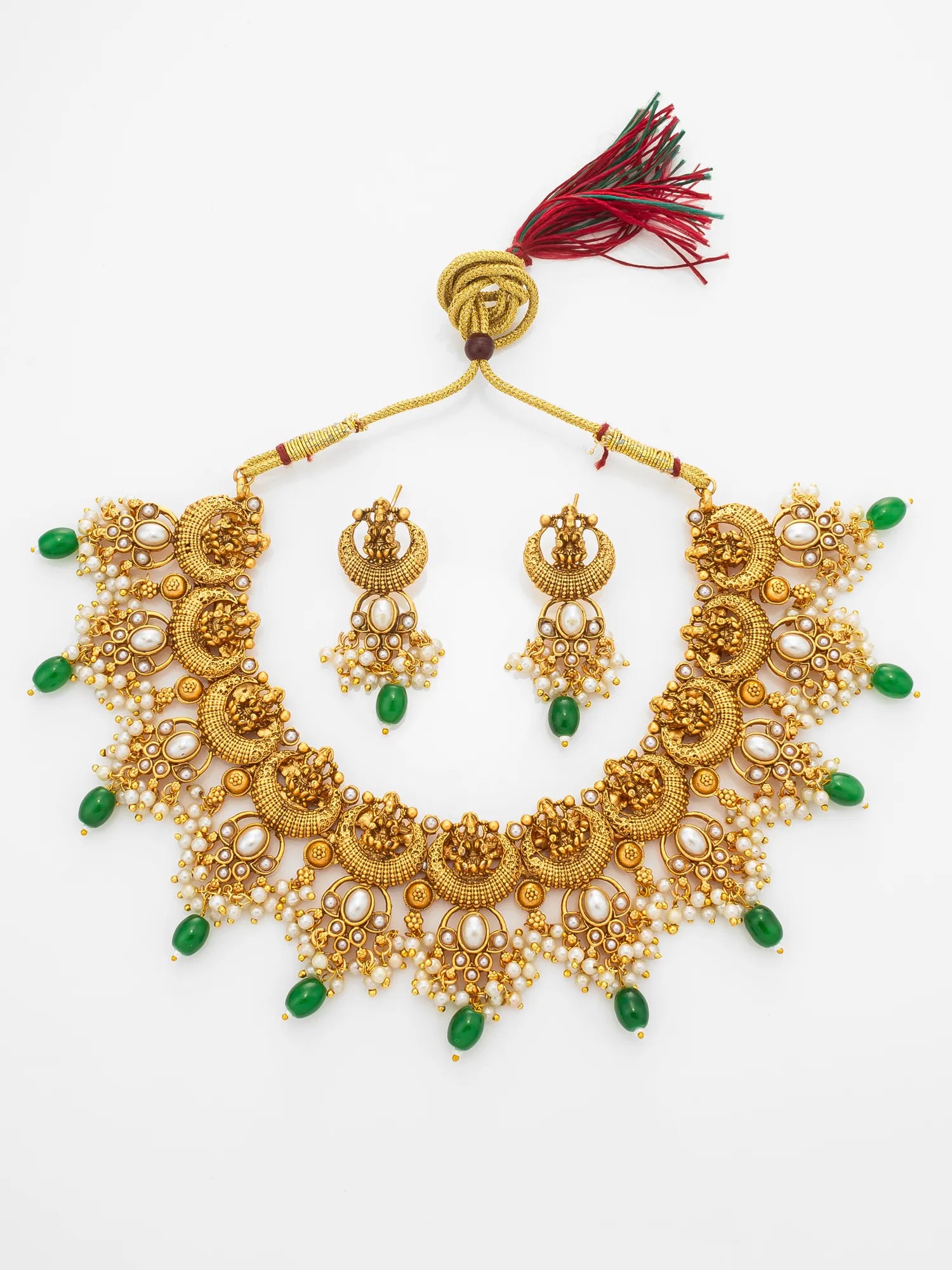 Gold-toned traditional jewelry set featuring a statement necklace and matching earrings, embellished with white pearl-like beads, green teardrop beads, and a red and black tassel, displayed on a white background.