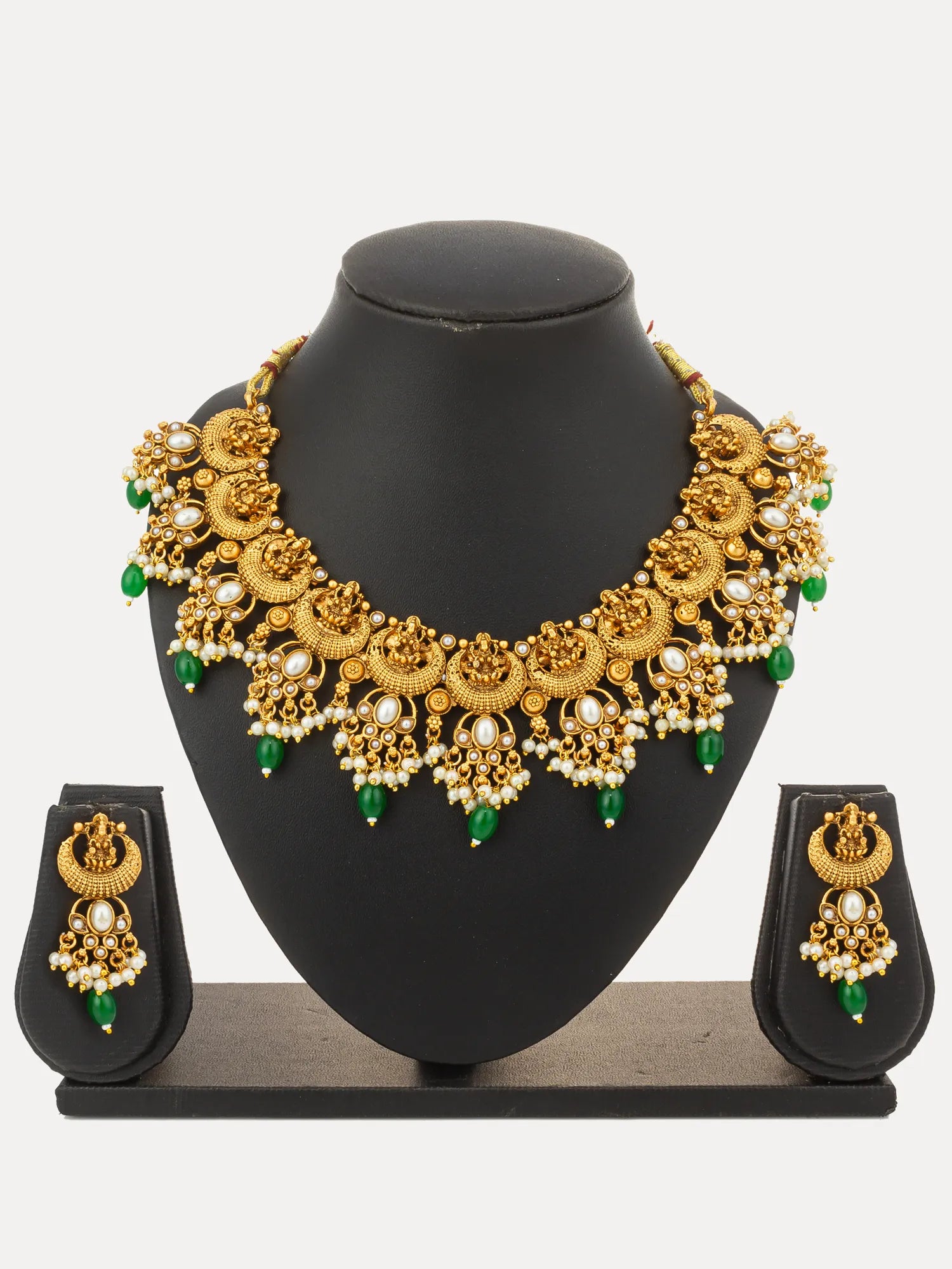 An ornate gold-toned jewelry set displayed on a black mannequin bust, including a wide collar-style necklace and matching drop earrings, decorated with gold filigree, white pearl-like beads, and green teardrop accents, against a light gray background.