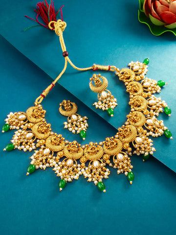 An ornate gold-toned traditional necklace set with matching earrings, decorated with white pearl-like beads, green stone accents, and a red tassel, arranged on a teal-blue background.
