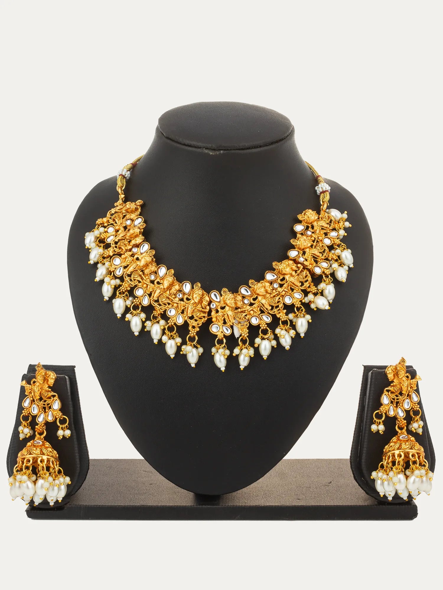 Gold-toned traditional jewelry set displayed on a black mannequin bust, including a statement necklace with dangling pearl-like beads and matching drop earrings on a stand.