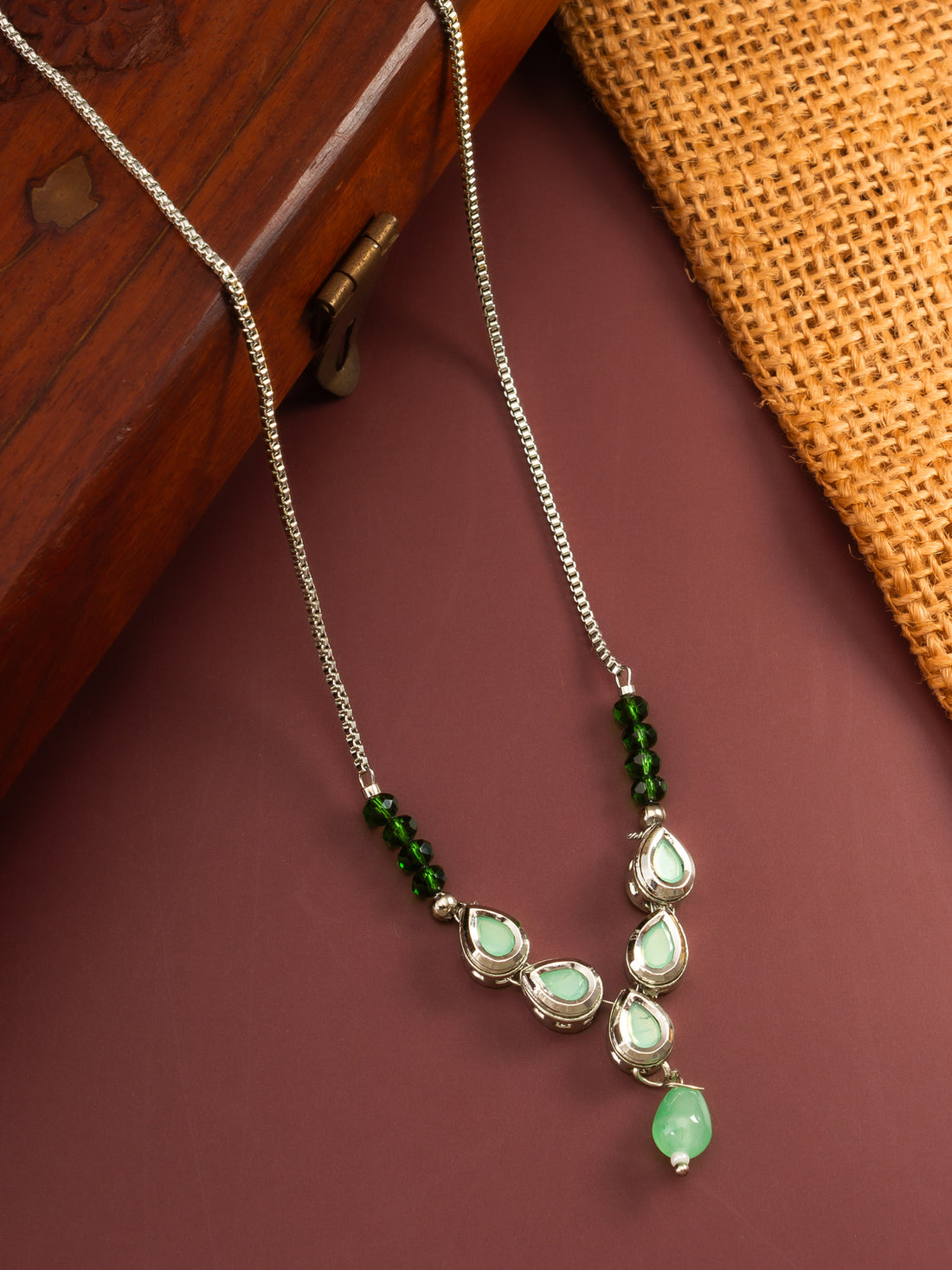 Close-up of a woman wearing a green gemstone necklace against a dark background
