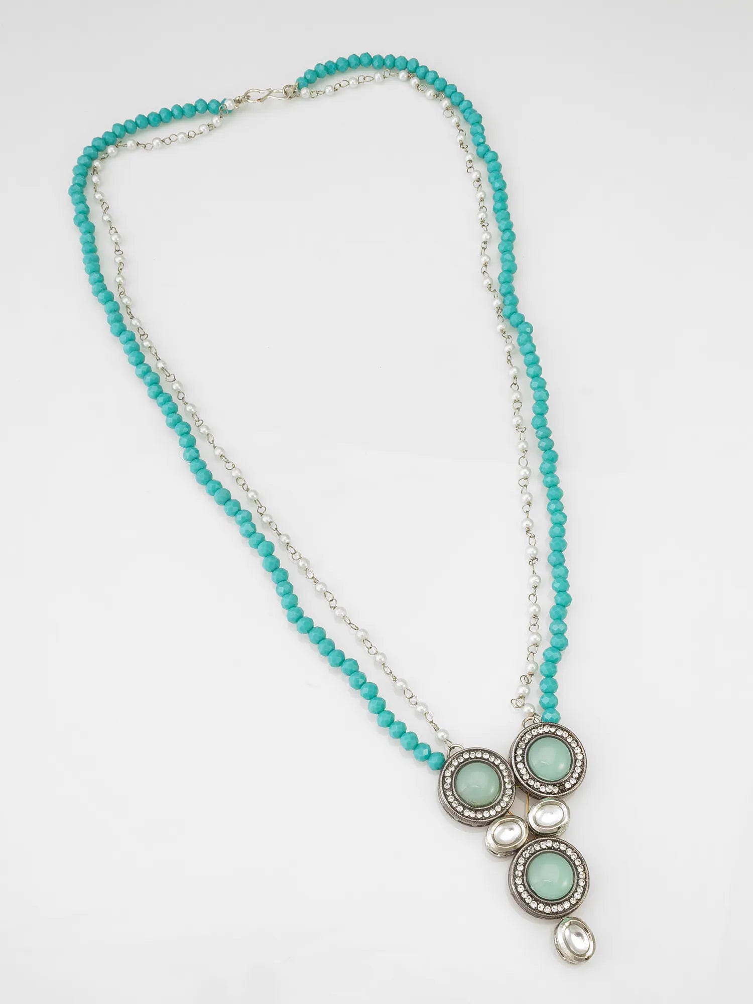 A long beaded necklace featuring a strand of turquoise blue beads and a silver-tone chain, with a central cluster of three oval light green stones surrounded by silver filigree and small pearl-like accents.