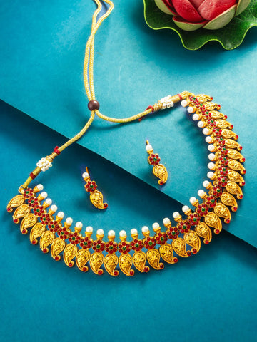Gold-toned traditional necklace and matching earrings with red and white bead detailing, arranged on a teal-blue background with a decorative flower in the corner.