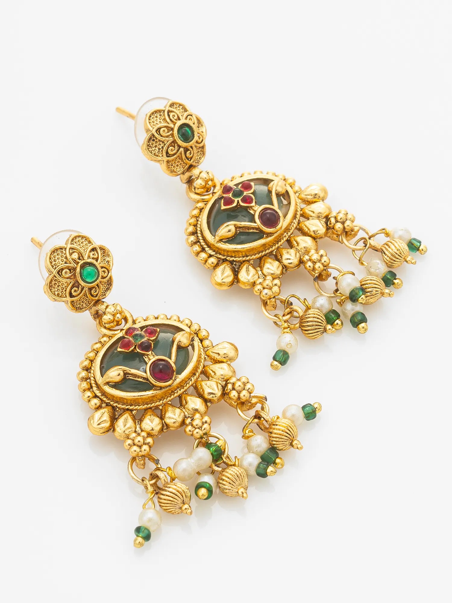 A pair of ornate gold-toned Indian jhumka earrings with green and red enamel details, white pearl beads, and small green and red stones, shown on a plain white background.
