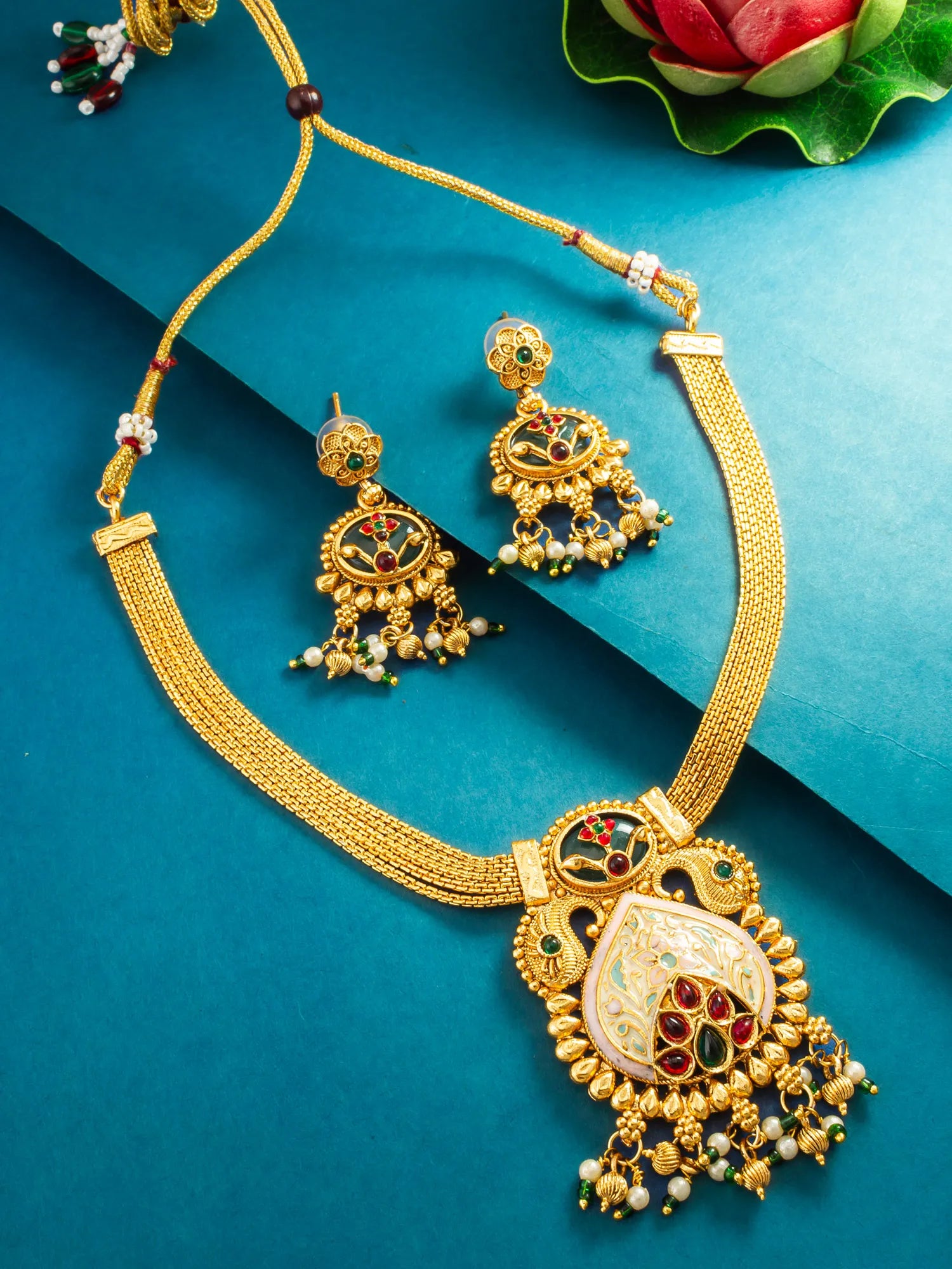 Gold-toned traditional jewelry set featuring a necklace and matching earrings with intricate multicolor enamel detailing, displayed on a teal background.