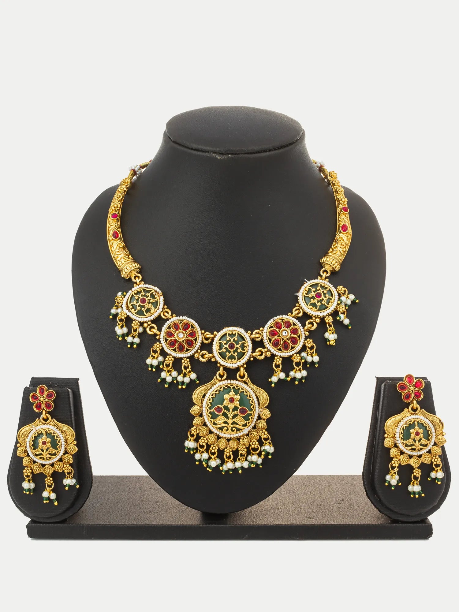 Gold-plated traditional Indian jewelry set featuring a statement necklace and matching earrings with green, red, and white enamel details, displayed on a black mannequin bust.