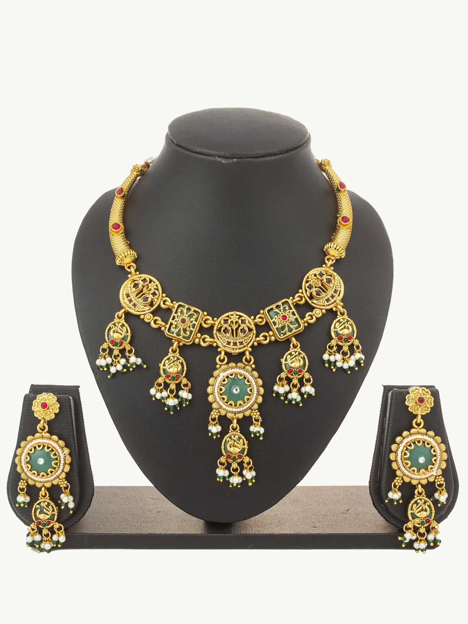 Gold-toned traditional jewelry set displayed on a black mannequin bust, including a necklace with dangling ornate charms and matching earrings with oval green and gold motifs.