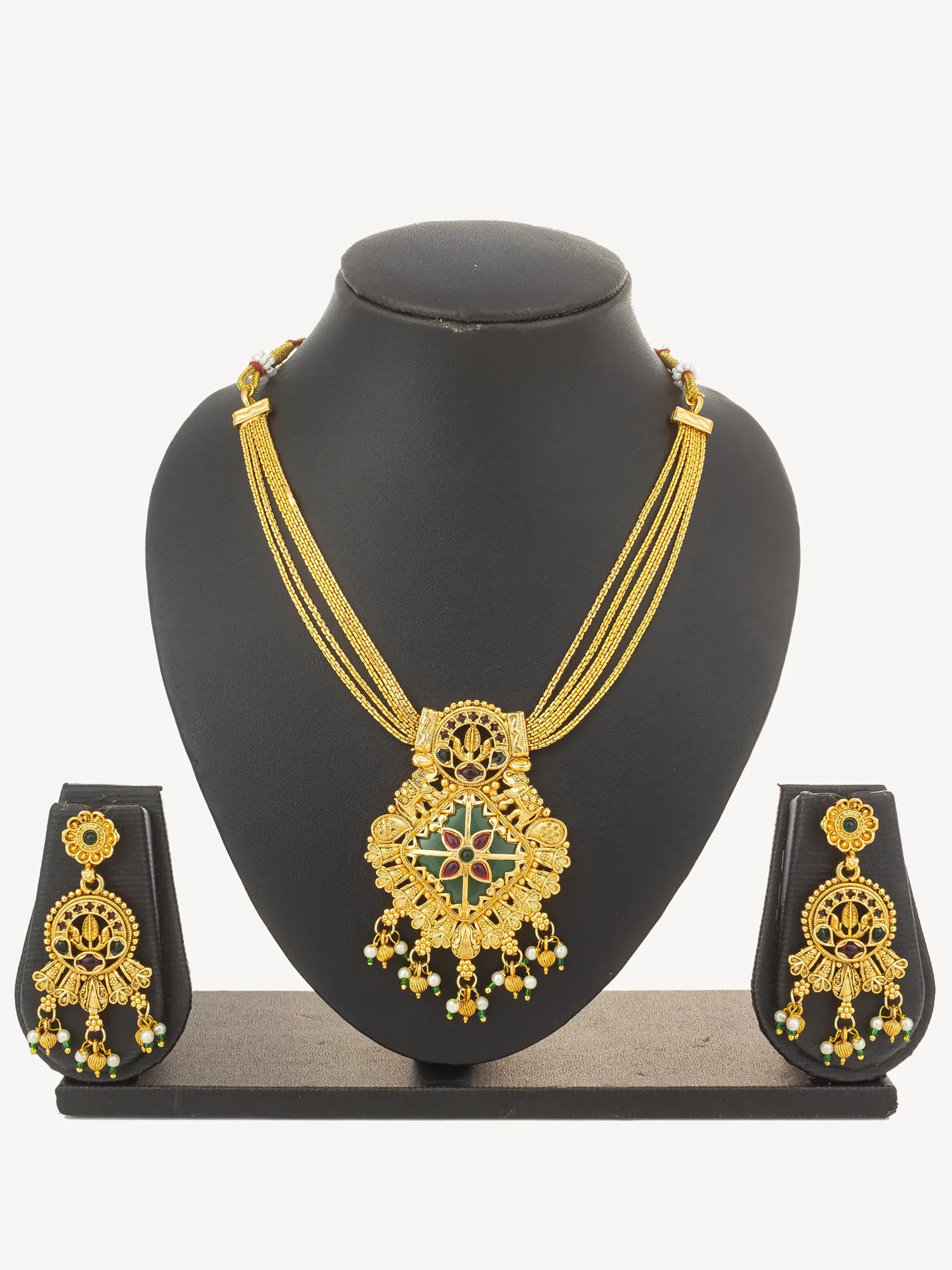Gold-tone traditional Indian jewelry set featuring a necklace and matching earrings with green and red enamel details and small bead accents, displayed on a clean black background.