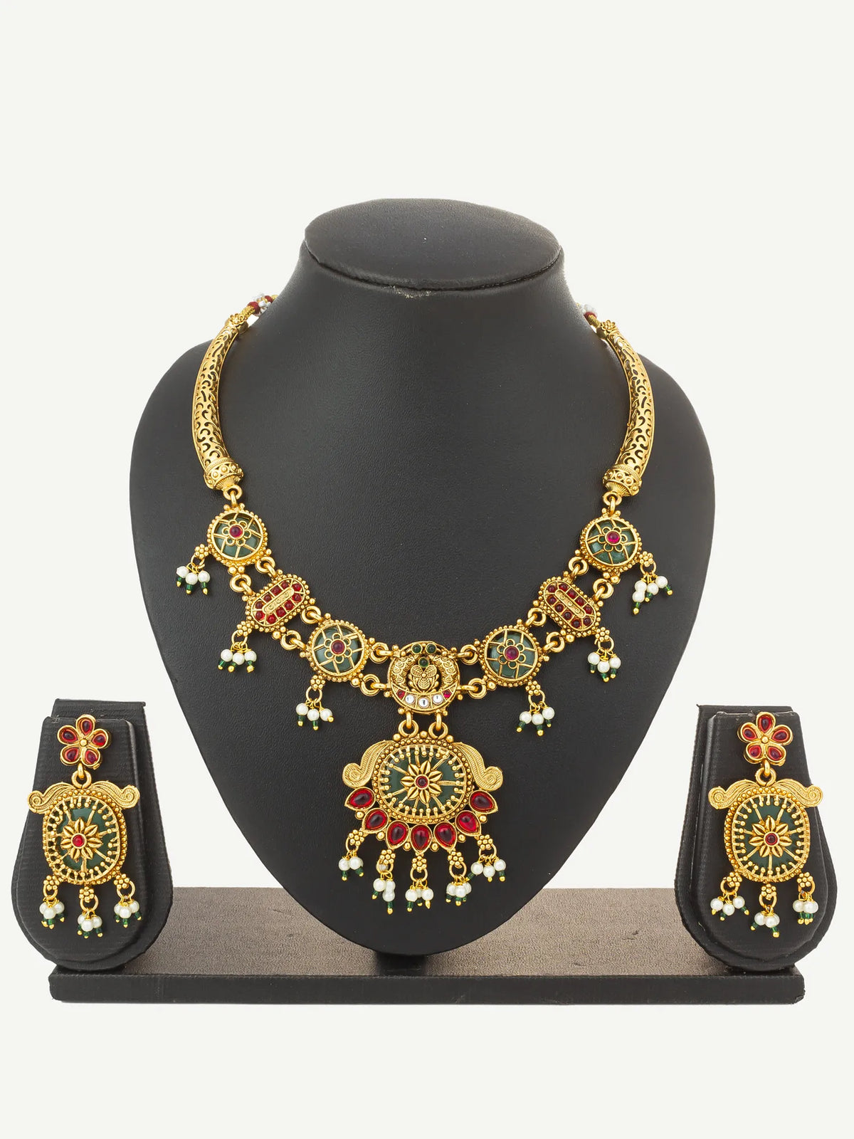 Gold-plated traditional Indian jewelry set featuring a statement necklace and matching earrings with red and green enamel details and white pearl-like accents, displayed on a black mannequin bust.