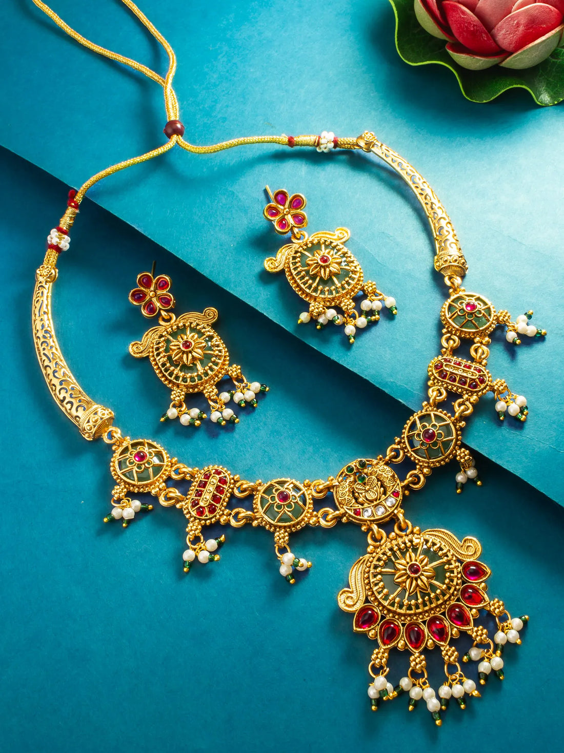 Gold-plated Indian jhumka necklace and matching earrings with red and green enamel details, set against a blue background.