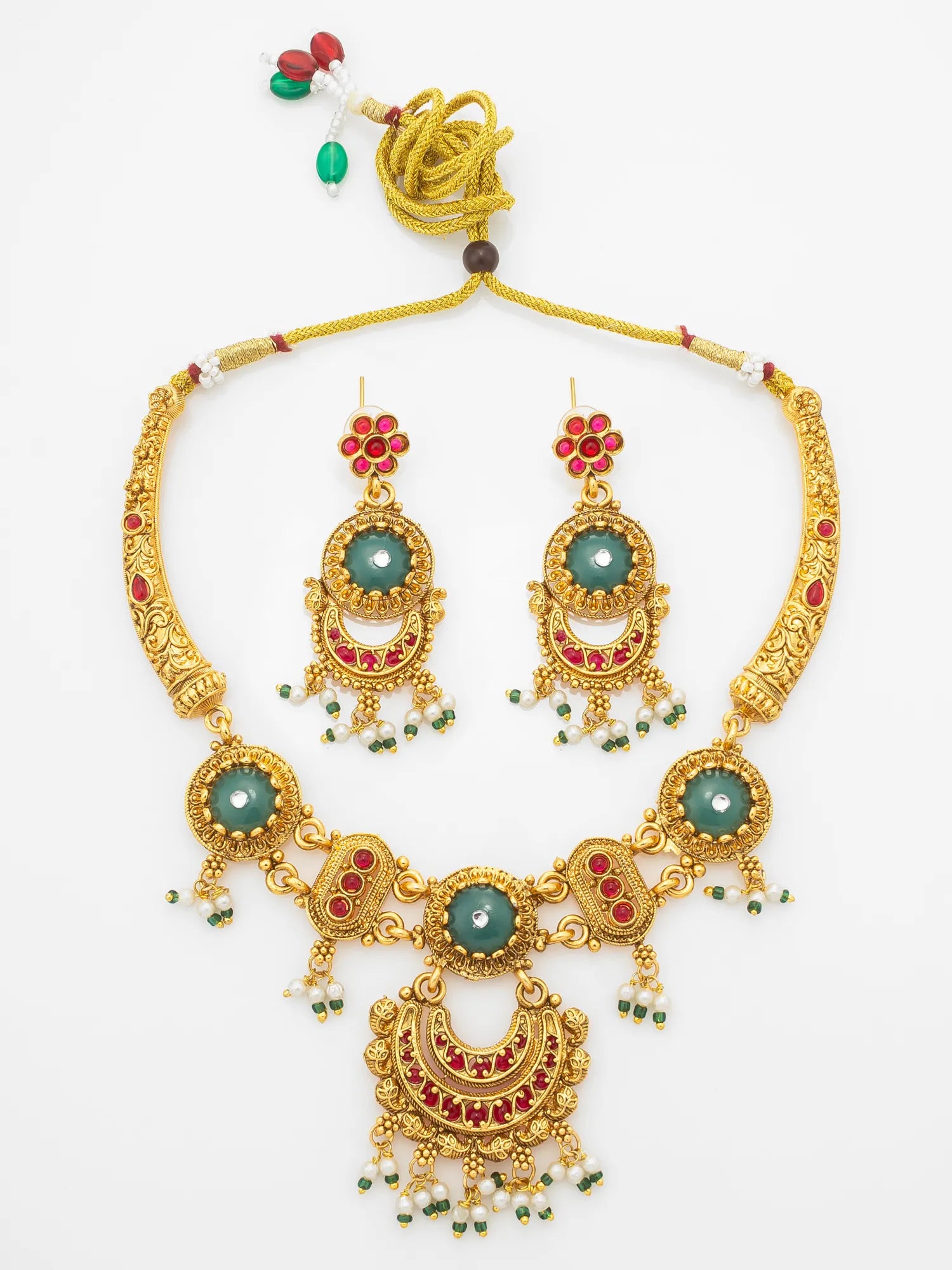 Gold-plated traditional Indian jewelry set featuring a necklace and matching earrings with green stone centers, red enamel accents, and small pearl bead drops, displayed on a clean white background.