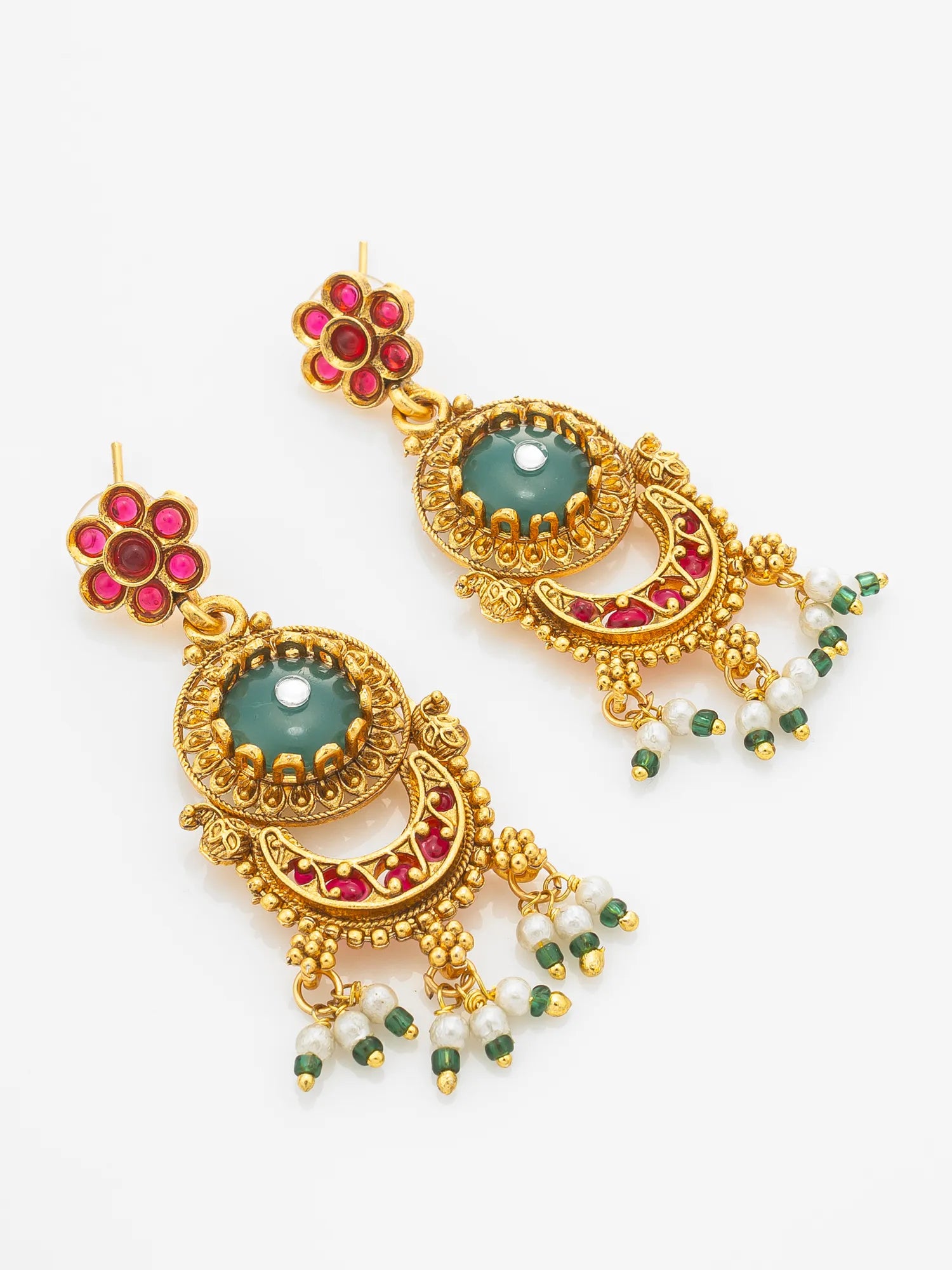 A pair of ornate gold-toned Indian jhumka earrings with green stone centers, red stone accents, and dangling white pearl beads, shown on a plain white background.
