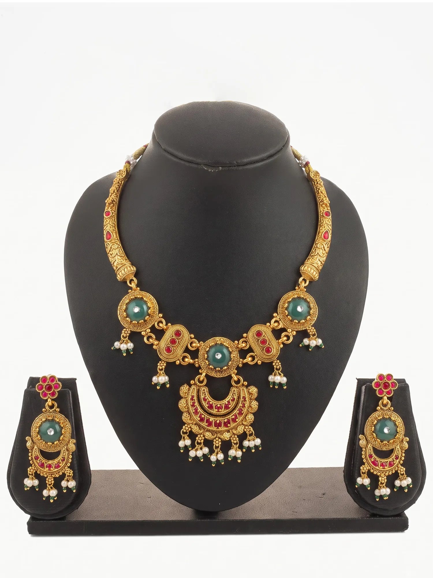 Gold-plated traditional Indian jewelry set featuring a statement necklace and matching earrings with turquoise green stones, red enamel details, and white pearl bead drops, displayed on a black mannequin bust.