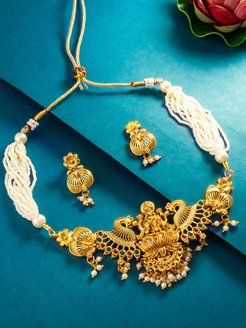 Gold-toned traditional Indian jewelry set featuring a necklace with a detailed peacock and floral pendant, matching earrings, and cream-colored beaded tassels, displayed on a textured blue background.