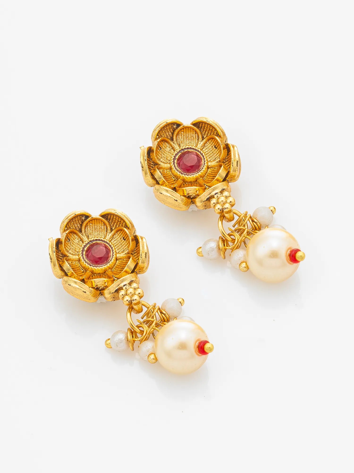 A pair of gold-toned traditional Indian earrings featuring lotus-shaped studs with red gemstone centers and dangling cream-colored pearls with small red accents, set against a plain white background.