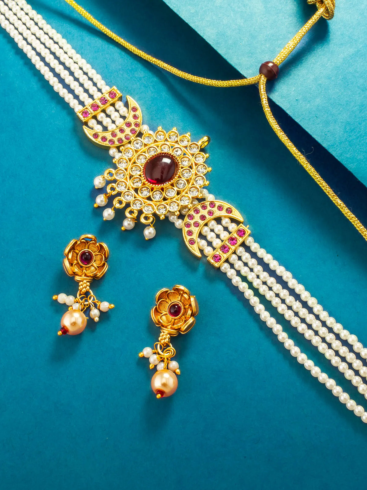 Gold and white pearl jewelry set featuring a multi-strand necklace with a central sunburst pendant, matching flower-shaped earrings, and a coordinating bracelet, arranged on a teal background.